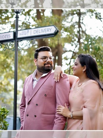 A casual and happy pre-wedding photo taken outdoors. The directional sign adds a fun, quirky element to the couple's portrait.