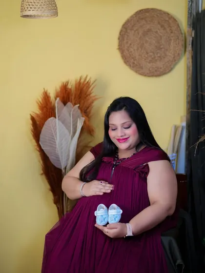 A sweet portrait focusing on the little things. The mom-to-be holds a pair of tiny blue booties over her bump, set against a warm, rustic background in our studio.
