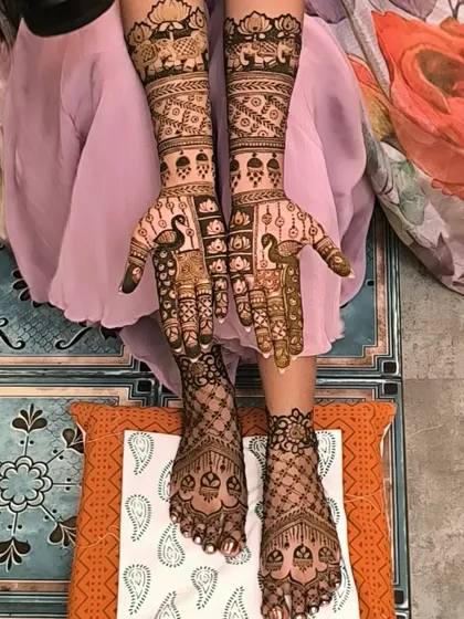 A complete bridal mehendi look, with detailed patterns covering the hands up to the elbows and full coverage on the feet. This design features classic peacock and jaali net patterns.