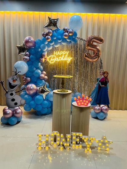 A 'Frozen' themed birthday decoration with an Olaf cutout, a blue and pink balloon arch over a shimmer curtain, and marquee letters for the name.