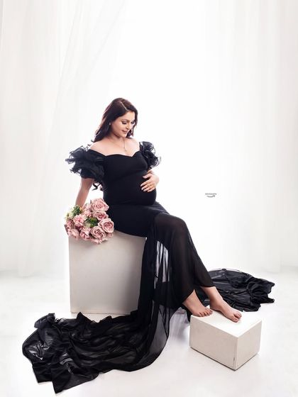 A quiet, contemplative moment captured in the studio. The client is seated in an elegant black gown, holding a bouquet of pink roses, creating a soft and romantic mood.