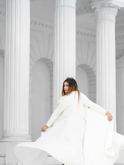 A dramatic, high-fashion shot with the model in a flowing white coat against white architectural columns. The monochrome palette creates a powerful and artistic image.
