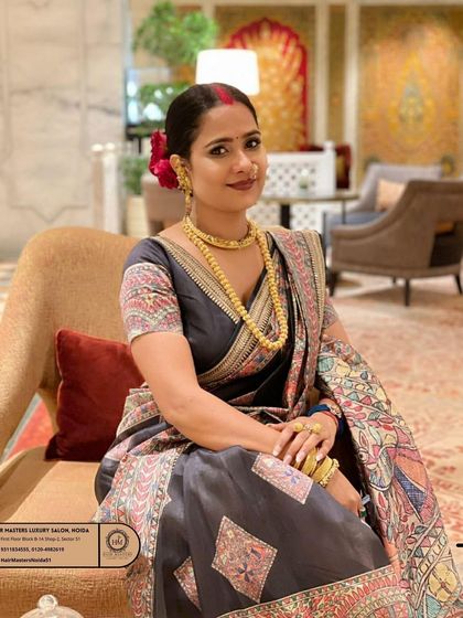 A beautiful, traditional look for a client in a printed saree. The makeup is classic with a red bindi and gold jewellery, and the hair is styled in a simple but elegant bun with flowers.