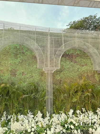 A detailed view of the custom wire mesh arches set against a wall of dense greenery. This image highlights the unique structural elements and the seamless integration of natural and man-made materials.