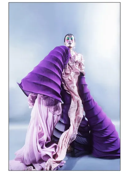 This image showcases the full volume and dramatic shape of the custom garment. The pose and flowing fabrics create a sense of powerful, contained energy.