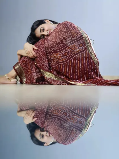 A cozy and intimate studio portrait. The reflection on the floor adds a layer of depth and artistry to this simple, beautiful shot of a model in a maroon saree.