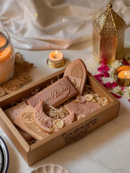 A wooden box filled with intricately decorated Eid cookies, shaped like moons, lanterns, and mosques. The detailed icing work makes these a beautiful and artistic gift.