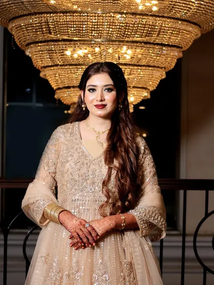This is a perfect example of a glamorous reception look. The makeup is bold yet elegant, with a classic winged eyeliner and a rich red lip that complements her sparkling gown. The soft curls and the grand chandelier in the background add to the royal vibe of the evening.