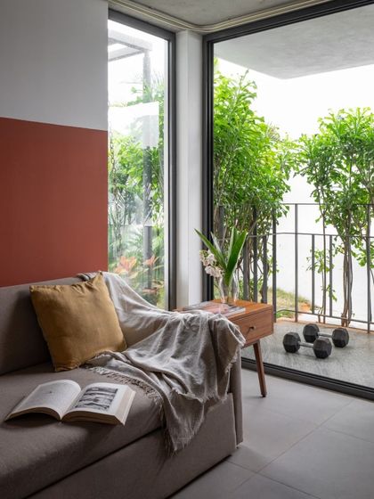 This cozy reading corner in a guest room features a daybed with a warm, rust-colored accent wall. The large glass door opens to a private balcony, blurring the line between indoor and outdoor space.