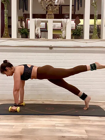 I incorporate simple tools to enhance our workouts and challenge the muscles in new ways. Here, I am using light dumbbells and ankle weights during a plank with a leg lift. This variation adds resistance to build greater stability in the core and strength in the glutes and legs.