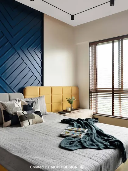 This bedroom showcases a bold design with a deep blue geometric accent wall and a contrasting yellow headboard. The neutral grey bedding and wooden blinds balance the look, creating a stylish and modern retreat.