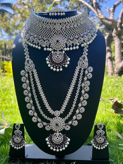 For a modern reception or sangeet look, this silver-plated CZ stone set with deep purple stones is a showstopper. It includes a choker, a multi-layered long necklace, and matching earrings, designed to catch the light and make you shine.