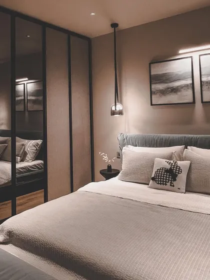 A moody and sophisticated bedroom design featuring a dark mirrored wardrobe that visually expands the space, paired with soft textiles and subtle accent lighting.