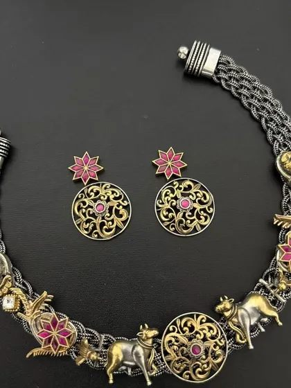 This custom fusion necklace set is a story in itself, featuring cow motifs, floral designs, and other traditional elements in a mix of oxidised silver and gold plate. The matching earrings complete the unique look.