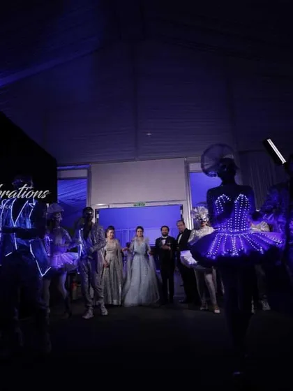 A wide shot of a sangeet entry, showing the couple about to enter a room filled with performers in glowing LED costumes. The anticipation and moody lighting create a dramatic effect.