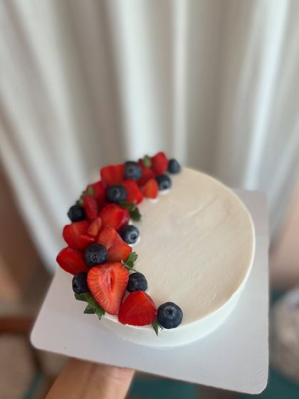 A minimalist cake design with a clean, smooth buttercream finish, accented with a crescent of fresh strawberries and blueberries.