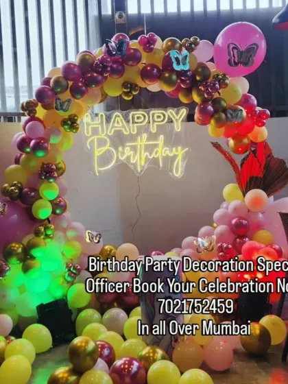 A vibrant and colorful butterfly-themed balloon ring. The mix of yellow, pink, and red balloons with butterfly accents and a neon sign makes for a very cheerful party decoration.