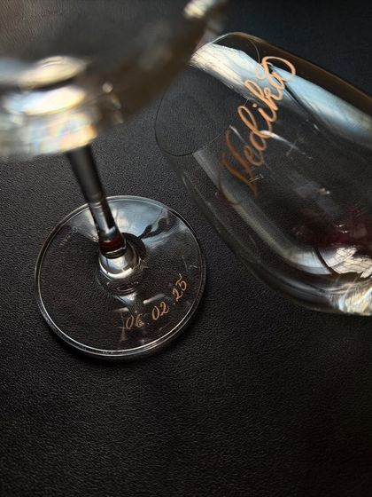 A close-up of a personalized wine glass, showing the name engraved on the bowl and the date on the base. These small details make beautiful gifts for couples.