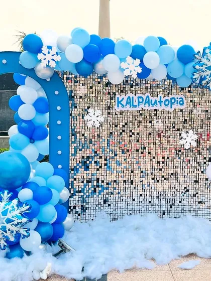 For the 'KALPAutopia' corporate winter event, we built a festive photo zone complete with a silver sequin wall, a custom branded sign, and a cheerful snowman prop. The blue and white balloon garland with snowflake accents completed the winter theme.