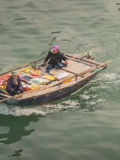 An aerial view of a small boat in Halong Bay, Vietnam, where vendors sell snacks to tourists on cruise ships, showcasing a unique form of local commerce.