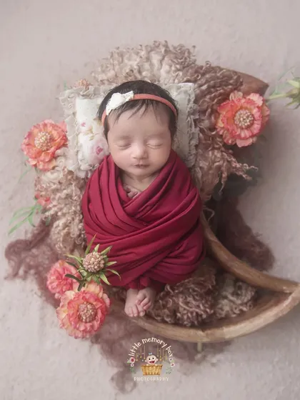 Wrapped in a deep red, this baby is surrounded by earthy tones and textures. This style of newborn photography creates a warm, rich, and artistic portrait.