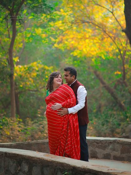 A happy and connected couple's portrait in the park. The vibrant red saree stands out beautifully against the autumn-colored leaves.