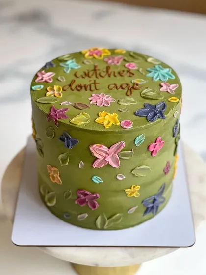 This olive green buttercream cake is covered in colorful, textured, hand-painted flowers. The message on top, "witches don't age," adds a fun and cheeky touch.