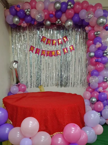 A simple balloon frame decoration for a first birthday, using purple, pink, and silver balloons around a cake table.