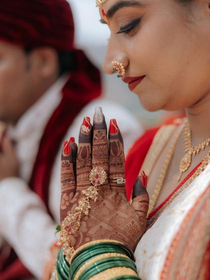 A close-up of the intricate details. The focus is on her beautiful henna, complemented by classic red nails and traditional jewelry, all part of the complete bridal look.