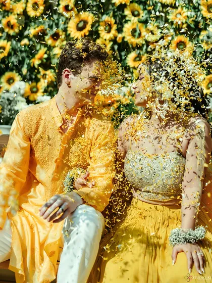 A playful moment as the couple is covered in flowers during their sunflower-themed Haldi, a beautiful and fun shot.