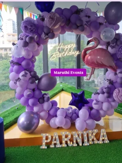 A unique flamingo-themed party. The circular balloon arch in shades of purple is accented with a large pink flamingo and a neon "Happy Birthday" sign.