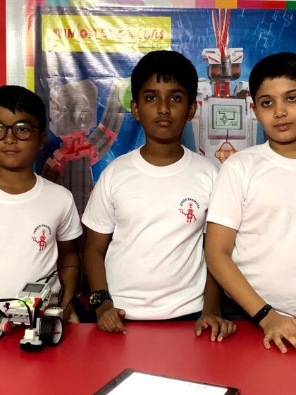 A team of three young engineers stands behind the robot they built and programmed together for a competition.