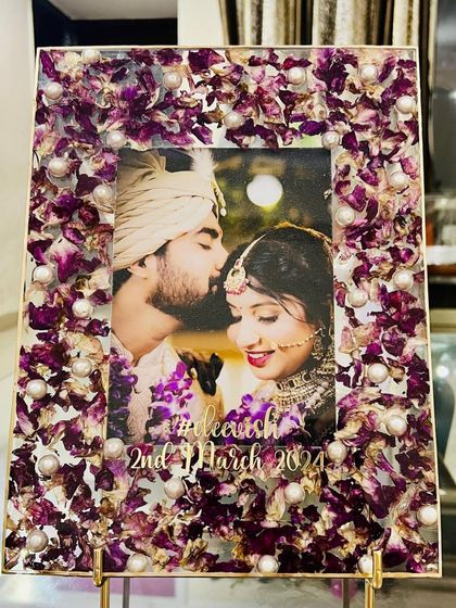 A beautiful rectangular photo frame made with preserved purple orchid petals and pearls. The couple's photo is surrounded by the delicate flowers from their wedding, creating a unique and personal keepsake.
