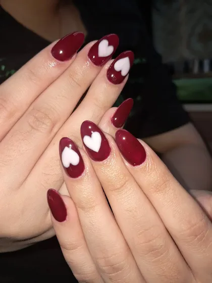 A bold and romantic design. These almond-shaped nails are painted in a deep red with crisp, white hearts on the accent nails for a classic Valentine's look.