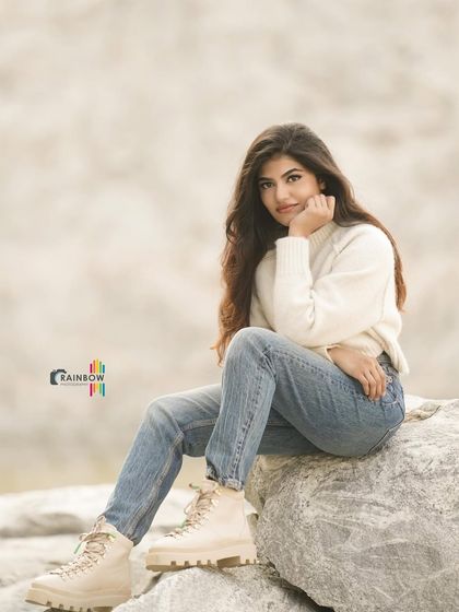 A casual winter look with a white sweater and jeans. The rocky, outdoor setting adds a rugged, natural element to the shoot.