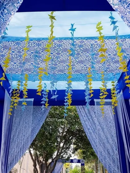 A view from inside the blue draped entrance tunnel, looking up at the patterned ceiling and hanging origami birds.