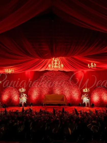 A royal red affair. This reception stage is bathed in dramatic red lighting, with a floral wall backdrop and elegant chandeliers creating a look of pure opulence and romance.