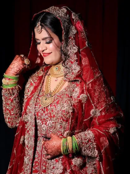 The elegance of a bride in red and gold. The makeup is designed to complement the heavy embroidery and jewelry without overpowering the bride's natural beauty.