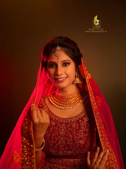 A classic bridal portrait from the same series, showing the full elegance of the red lehenga and veil. The soft lighting and her gentle smile create a timeless image that is perfect for any wedding album.