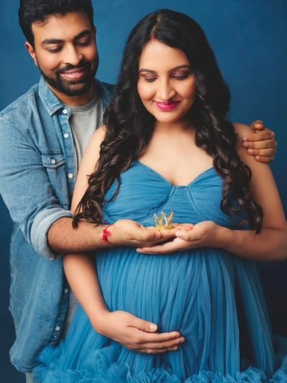 A loving couple's portrait, with the mom-to-be in our blue ruffled gown, holding tiny shoes in anticipation of their new arrival.