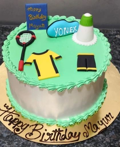 A badminton-themed cake for a sports lover. The cake is decorated with an edible racket, shuttlecock, and sportswear, all on a green "court."
