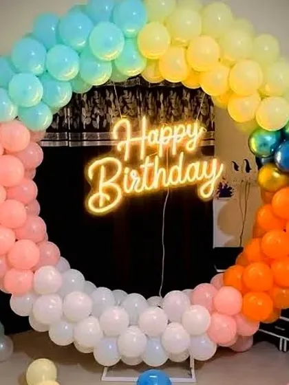 A popular choice for birthdays is this ring balloon decoration with a rainbow color scheme and a central 'Happy Birthday' neon sign. It's a simple yet very effective backdrop for cake cutting.
