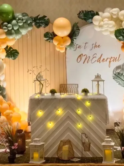 A fun jungle safari theme for a "ONEDERFUL" first birthday. The decor features a balloon arch with green and orange tones, monstera leaf accents, and cute animal props like a giraffe.