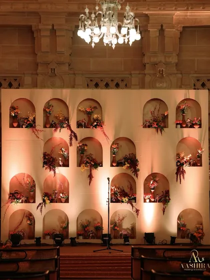 A unique stage backdrop created from a wall of niches, each holding a small, artistic floral arrangement, lit from below to create a dramatic effect.