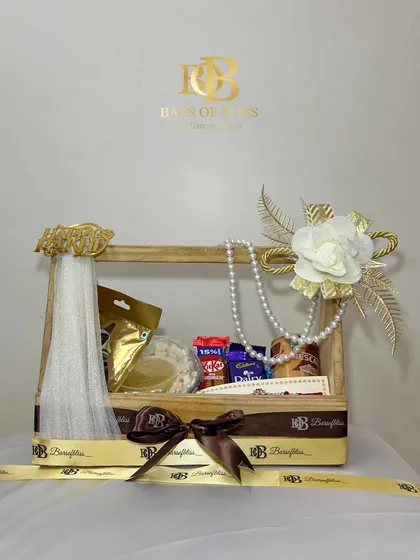 Elegance in a crate. This Raksha Bandhan hamper combines treats and tradition, featuring a caramel swirl cake, assorted chocolates, a coffee can, and a beautiful rakhi, all arranged in a reusable wooden crate decorated with pearls and flowers.