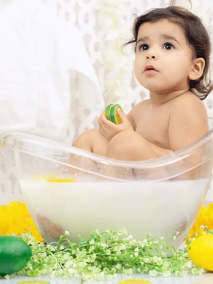 A baby looks up with curiosity while sitting in a milk bath filled with lemon and lime slices. A refreshing and unique photoshoot idea.