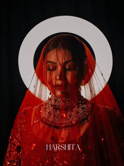 A creative and artistic bridal portrait. The halo light behind her and the red veil create a divine, almost saintly image. This is a modern, high-concept take on bridal photography.