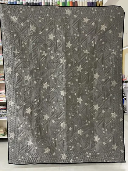The back of the Twisted Geese quilt, featuring a fun grey fabric with white stars.