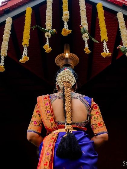 A beautiful shot focusing on the back of the bride, showcasing her intricate hairstyle with fresh flowers, traditional jewelry, and the detailed blouse of her saree.