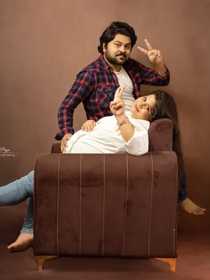 A fun and casual maternity portrait of a couple. They strike a playful pose on a sofa, showing that maternity shoots can be relaxed and reflect your personality.